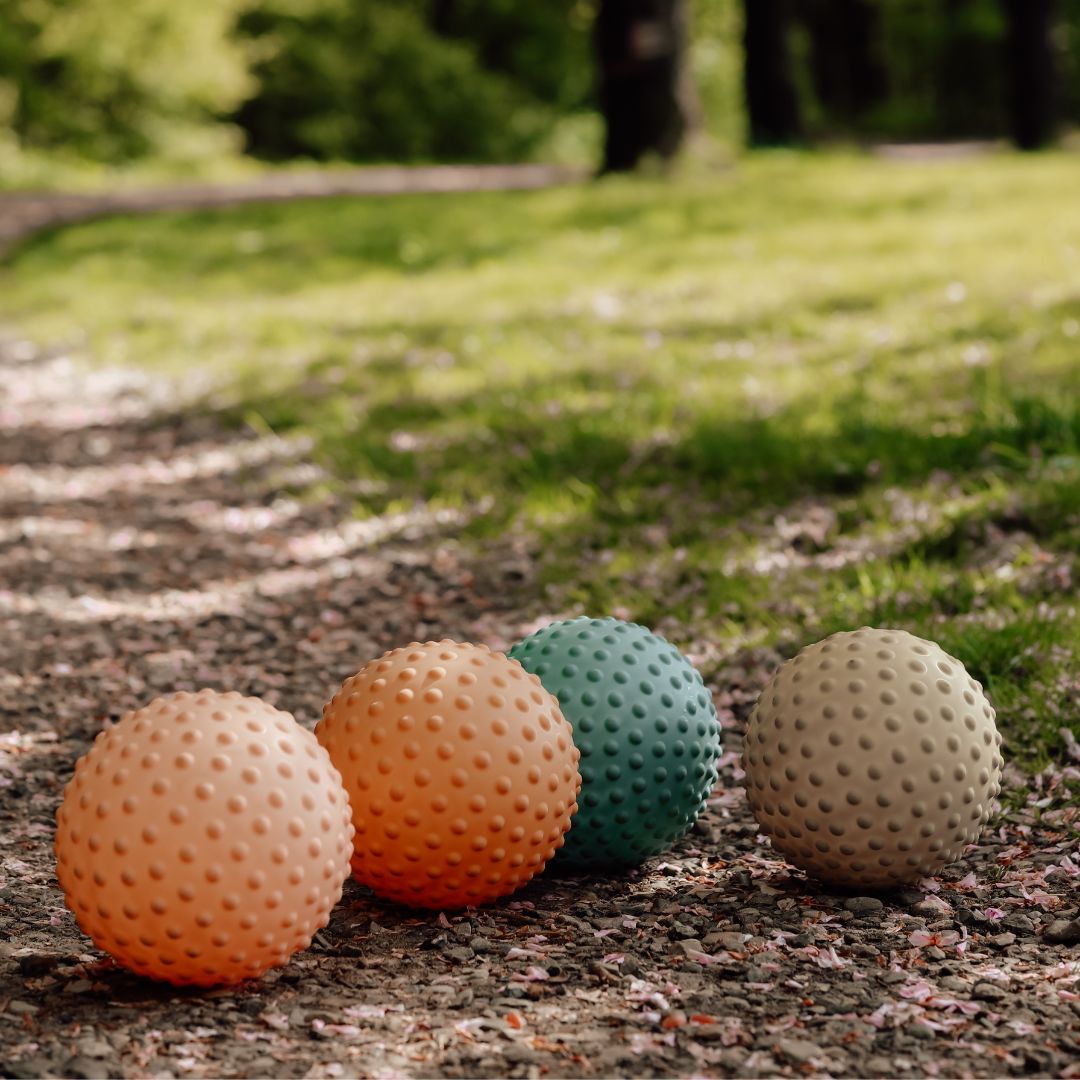 Farverige sansebolde med knopper på grusvej, perfekte til motorisk leg og sansestimulation for børn.