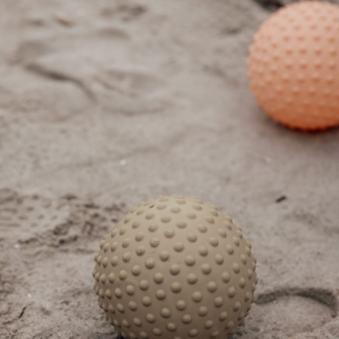 Grøn og orange sansebold i sand, med noprede overflader til sansestimulation og motorisk leg for børn.