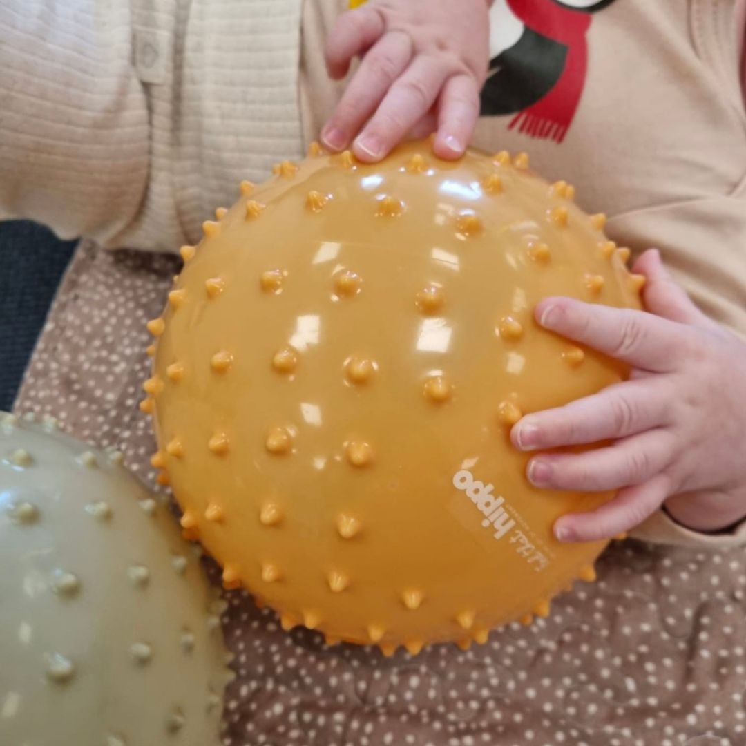 babyhænder på stor gul sansebold med knopper hos Nordic Simply