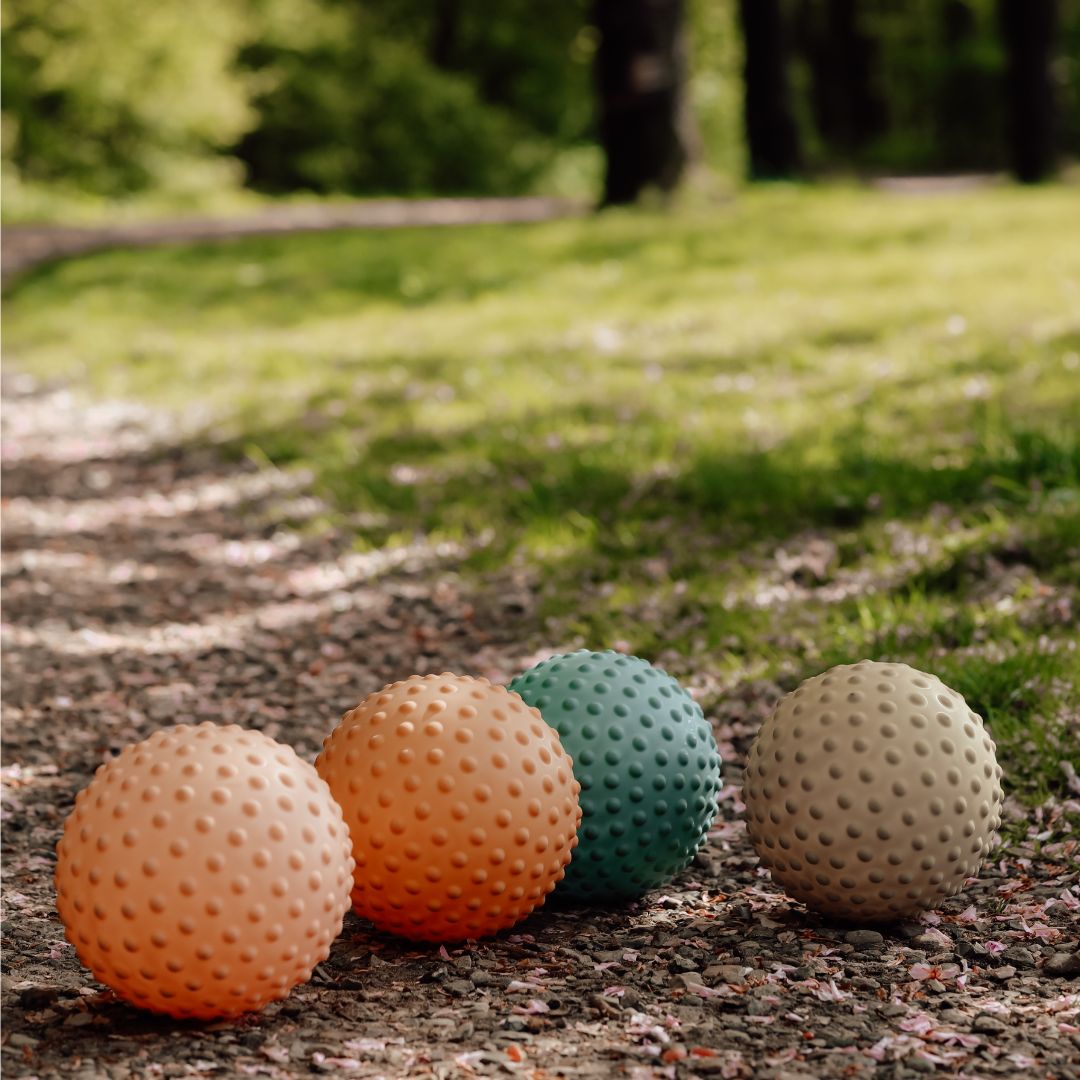 Farverige sansebolde i mat finish med knopper ligger i naturen, perfekte til babyer og børn til sanseleg.