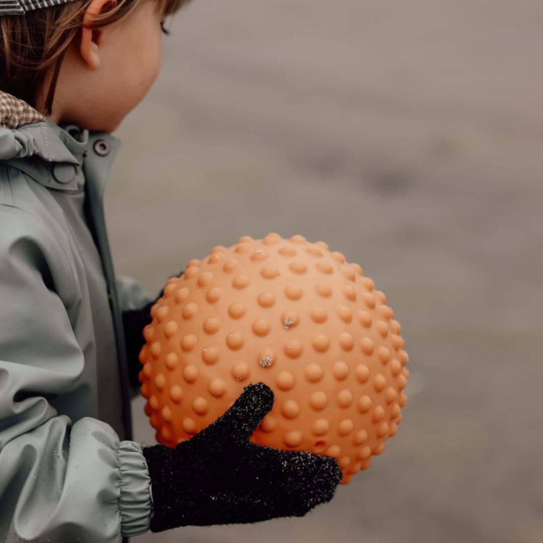 Barn i regntøj, holder stor orange sansebold, ideel til sansestimulation og motorisk udvikling.