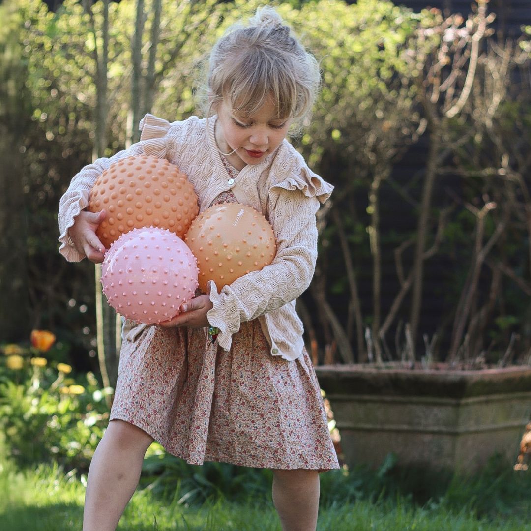 Pige leger i have med orange sansebold og flere sansebolde i forskellige størrelser