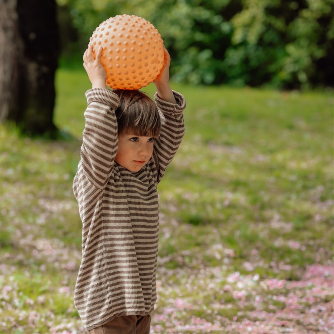 Barn leger med stor orange sansebold, ideel til sansestimulation og motorisk udvikling.