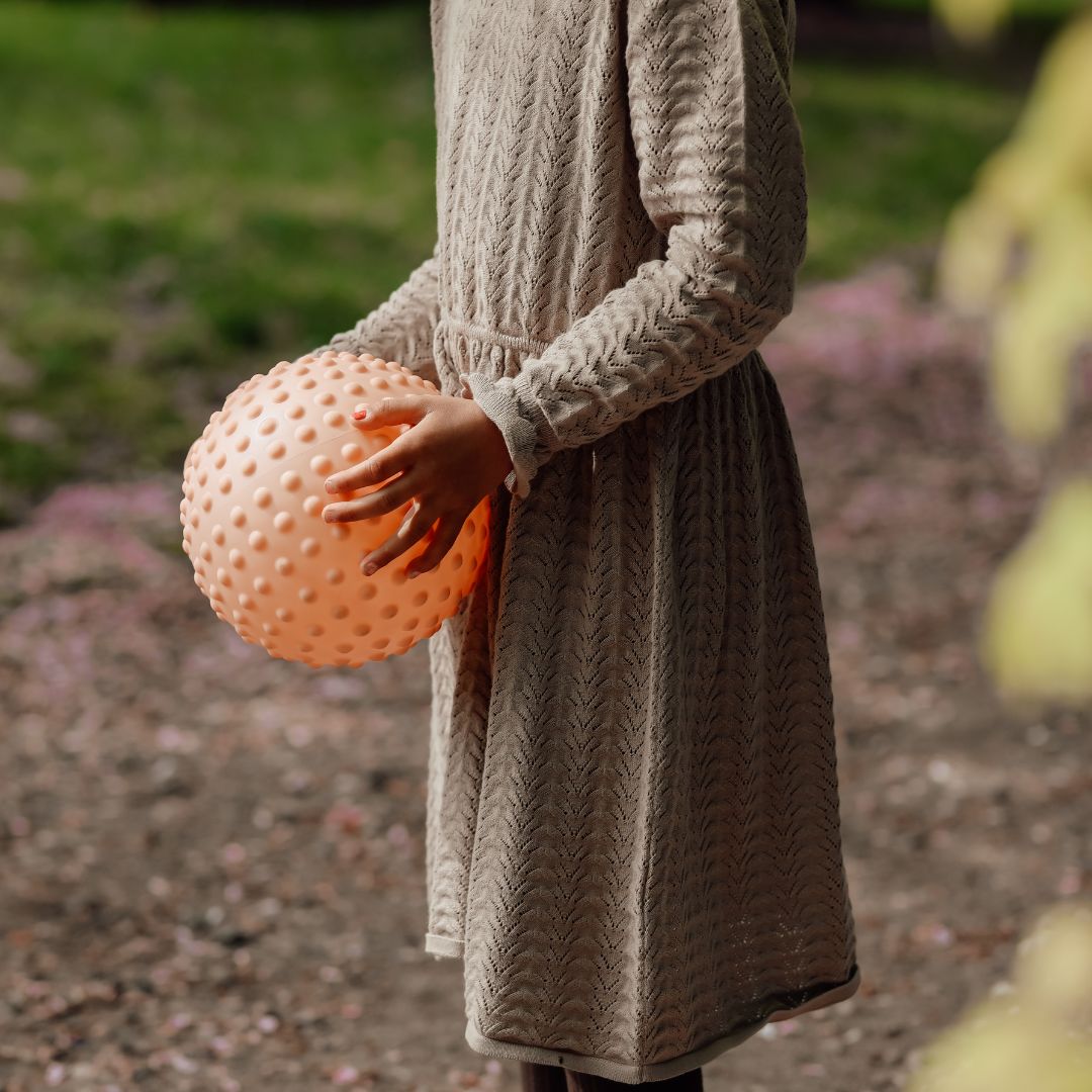 Barn holder en stor, rosa sansebold med knopper, ideel til sansestimulering og leg.