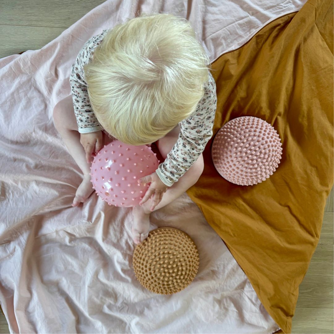 baby set oppefra med rosa sansebold og lyse sansesten der ligger på dyne fra Find that Hippo hos Nordic Simply