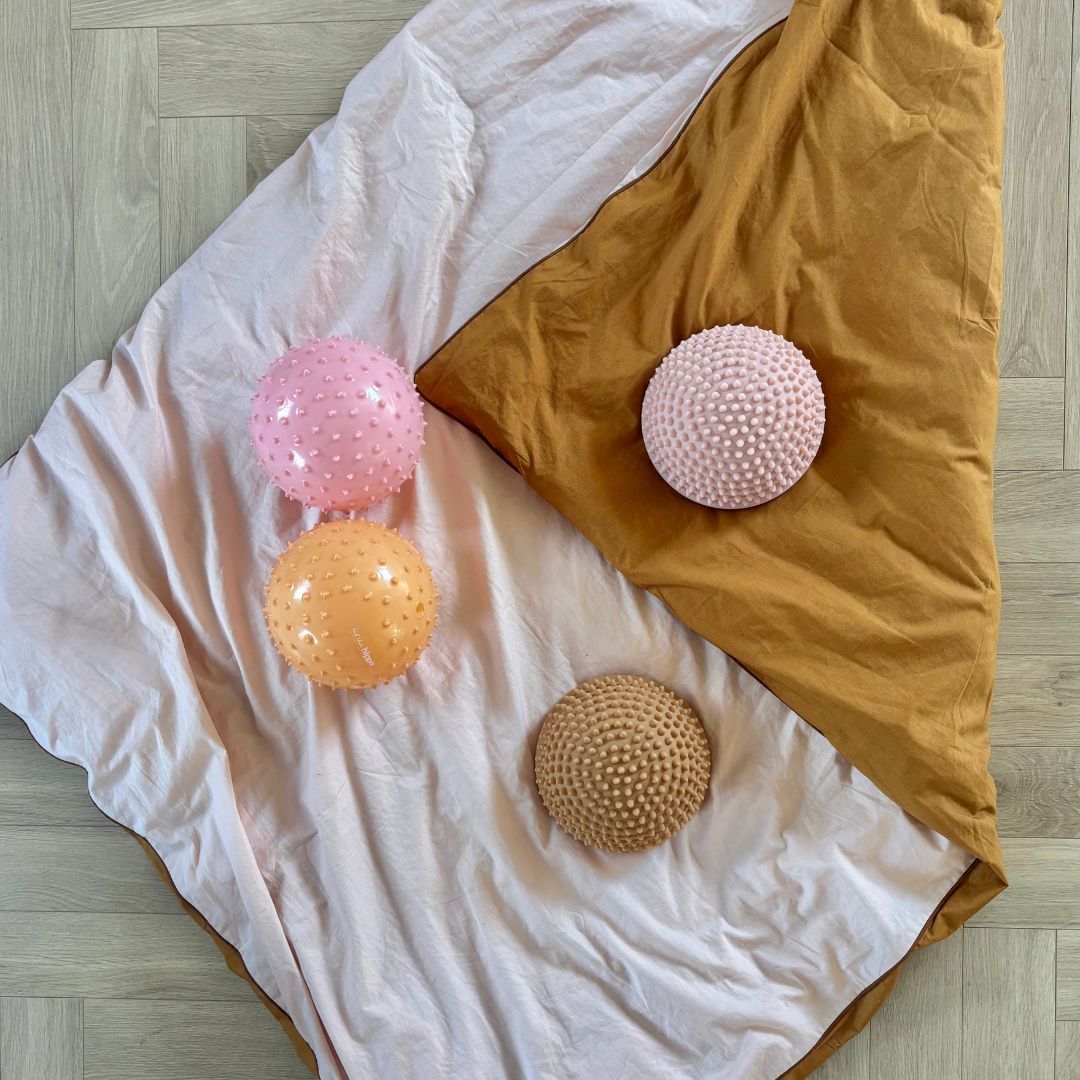 to sansebolde i rosa og orange samt to lyse sansesten fra Find that Hippo, set oppefra ligger på dyne, hos Nordic Simply