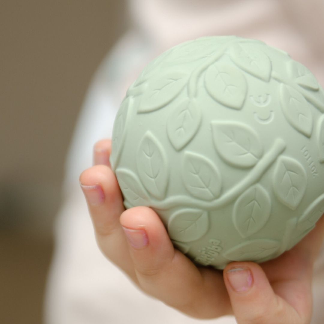 Hånd holer grøn sansebold i naturgummi med teksturer, fra Natruba, fås hos Nordic Simply