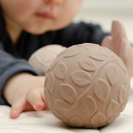 Baby rækker ud efter brun sansebold i naturgummi med teksturer, fra Natruba, fås hos Nordic Simply