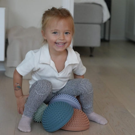 pige leger i stue med fire sansesten i mørke pastelfarver fra Find that Hippo fås hos Nordic Simply