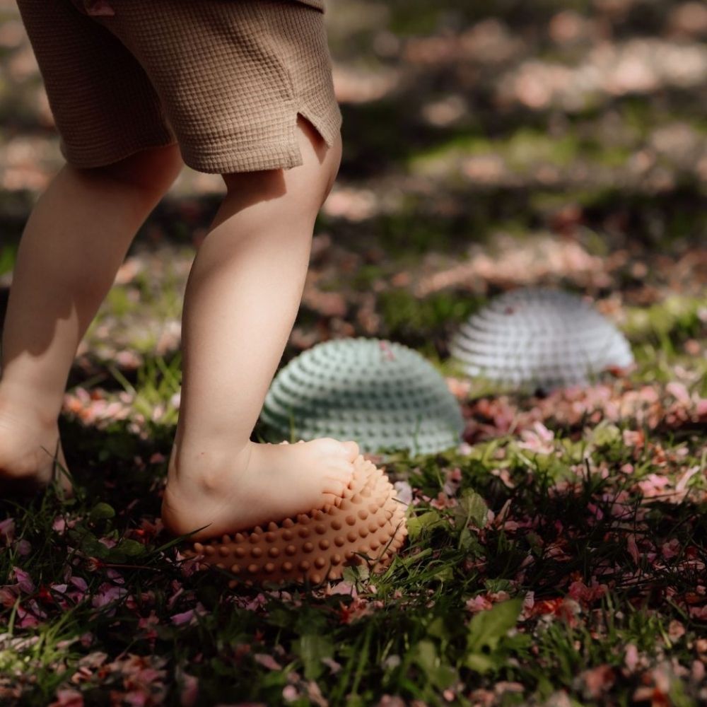 barn går med bare fødder på sansesten i pastelfarver med knopper, der ligger på en skovbund, fås hos Nordic Simply