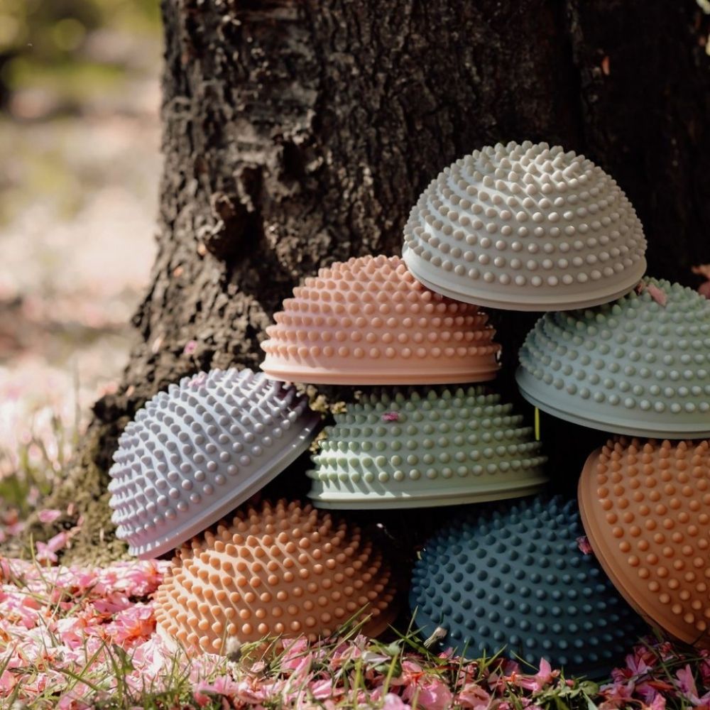 bunke af 8 sansesten med knopper i pastelfarver ligger op ad træstamme i skovbund med rosa blade
