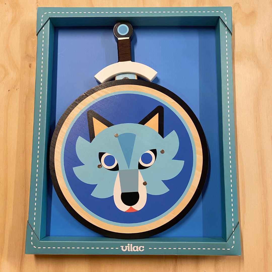 Æske med rundt skjold i træ med blå baggrund og motiv af ulv, nedenunder ligger svær i træ sæt med skjold og sværd til børn fra Vilac fås hos Nordic Simply