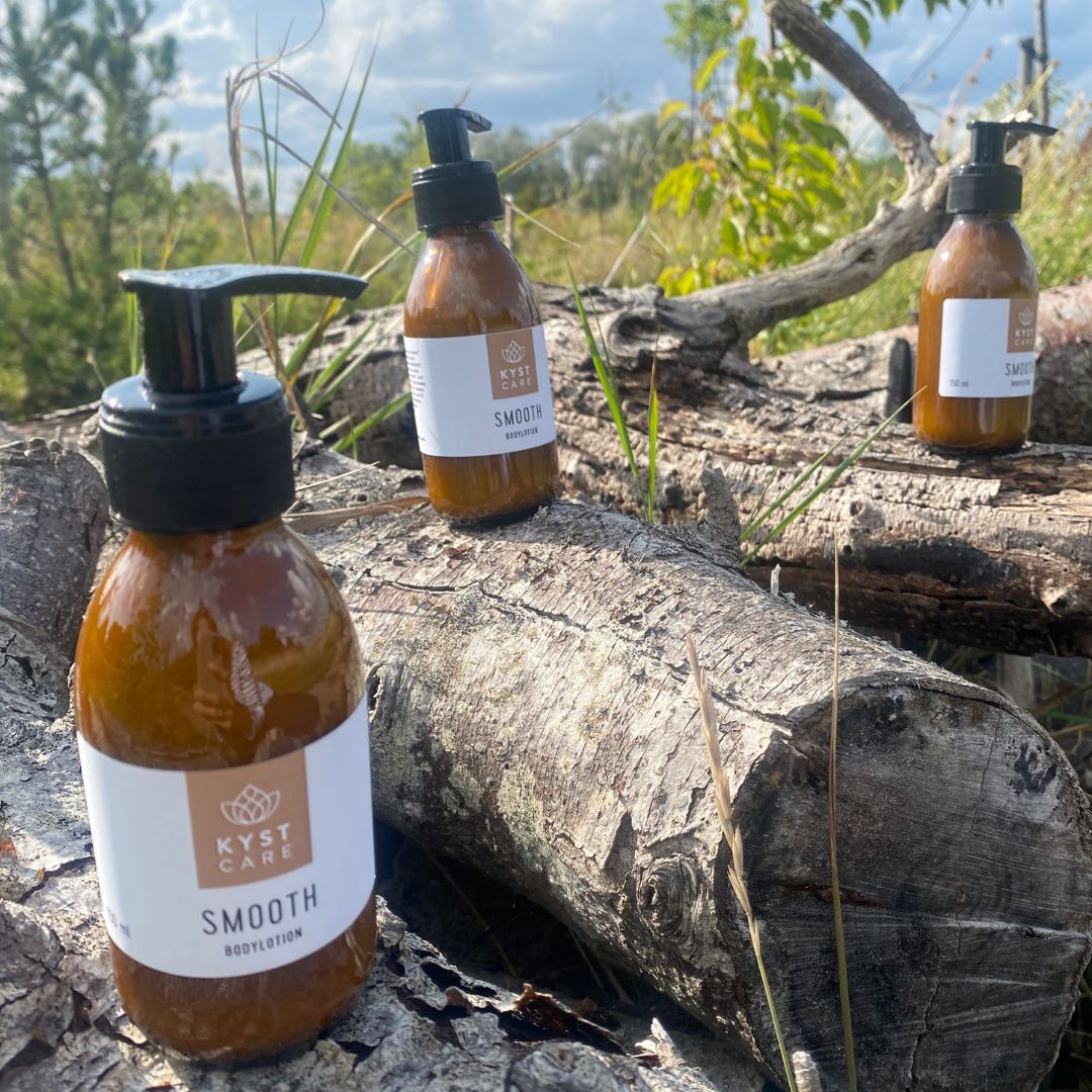 Tre flasker smooth bodylotion, fra danske Kyst Care, står på træstub, fås hos Nordic Simply