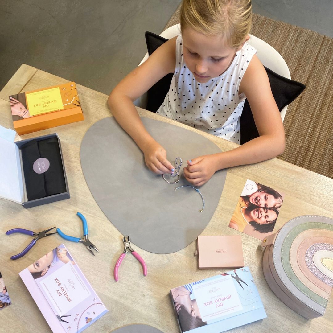 Pige ved bord laver DIY smykker, på bord ligger smykkeværktøj 3 forskellige tænger i lilla, rosa og blå til smykkefremstilling fra danske Me & My Box fås hos Nordic Simply.