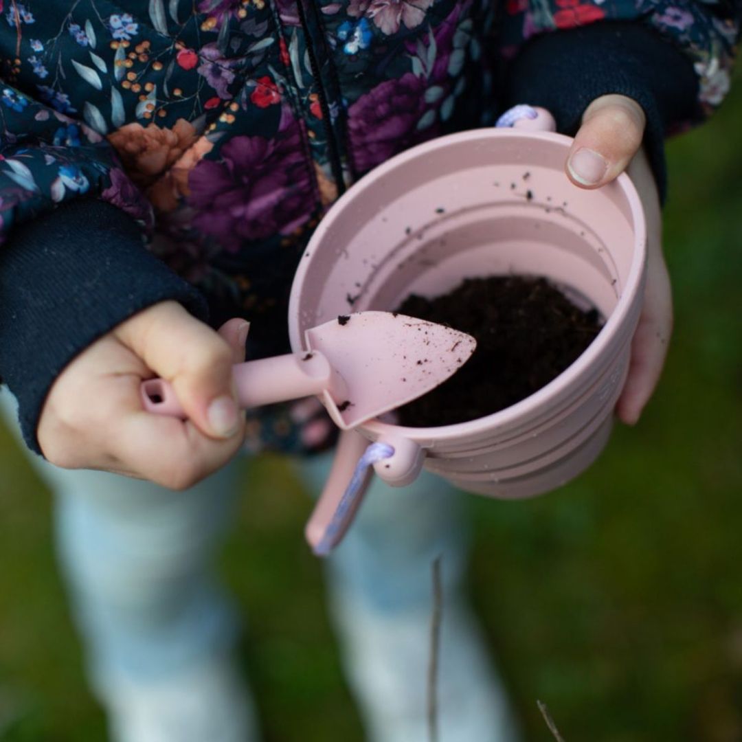 Hænder holder lille rosa spand med jord i, og mini skovl fra Scrunch, fås hos Nordic Simply