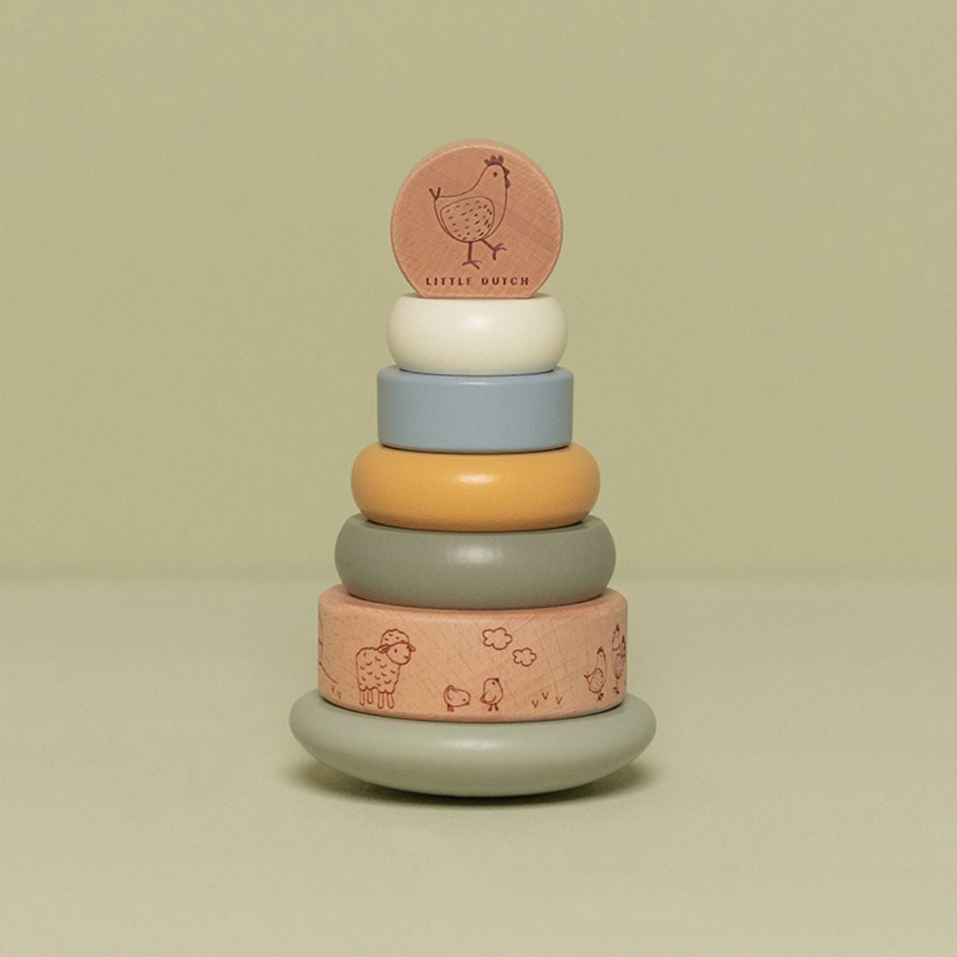 Stabeltårn med 6 stabelringe i lys blå, grøn beige farver med bondegårdstema set på grøn baggrund. Stabletårn i træ fra Little Dutch godt til hånd-øje koordination og finmotorik fra 12 måneder og op, fås hos Nordic Simply.