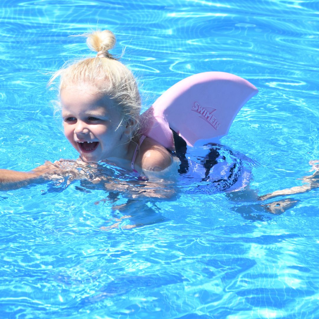 Pige i pool med rosa SwimFin hajfinne på ryggen. Original SwimFin fås hos Nordic Simply