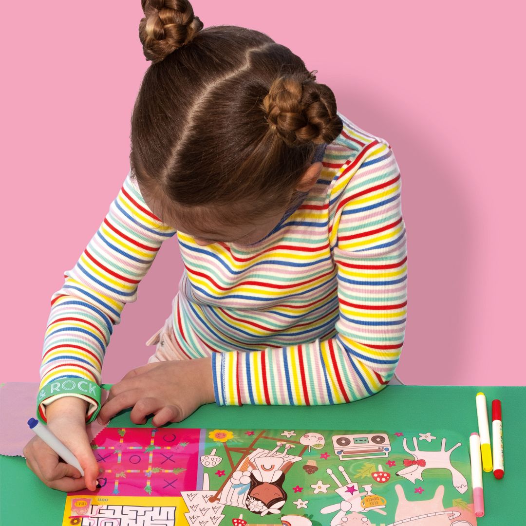 Pige tegner på farverig tegnemåtte med regnbuer og feer, perfekt til kreativ leg og fordybelse hjemme og på rejsen