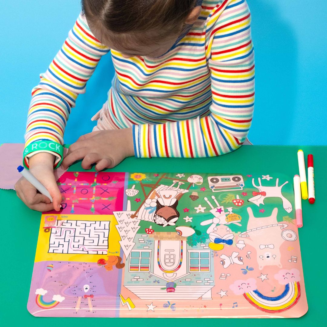 Pige ved grønt bord tegner på farverig tegnemåtte med regnbuer og feer, perfekt til kreativ leg og fordybelse hjemme og på rejsen , fås hos Nordic Simply