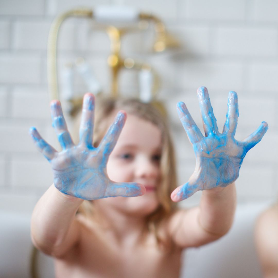 Pige viser blå hænder frem, farvet af pingvin tryllekugler til badet fra Tinti, fås hos Nordic Simply