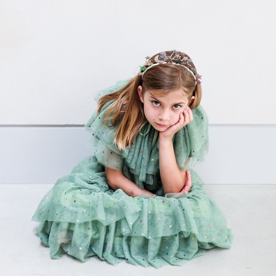 Pige sidder i udklædning som juletræ, med kort grøn kappe og langt grønt tylskort med flere lag og masser af stjerner, fra Mimi & Lula fås hos Nordic Simply