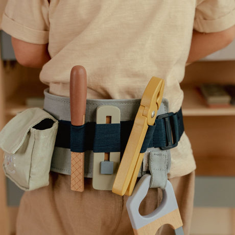 Barn med værktøjsbælte med stropper hvori der siddder legeværktøj i træ, her ses fil, knibtang, hobbykniv og sav der hænger nedad benet, fra Little Dutch, perfekt til rolle og fantasileg, fås hos Nordic Simply