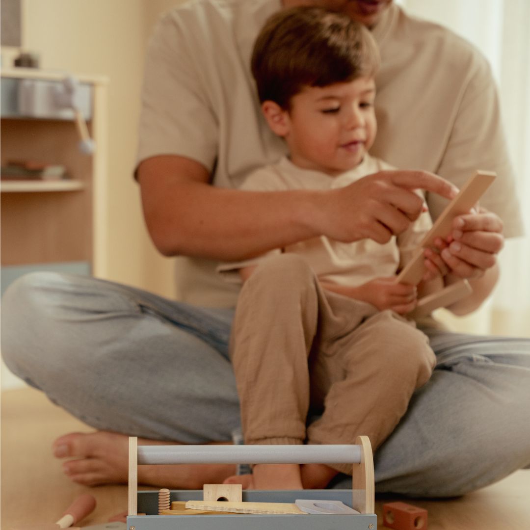 Far og søn leger med værktøjskasse i træ, hvor de bruger små værktøjer til sjov og læring.