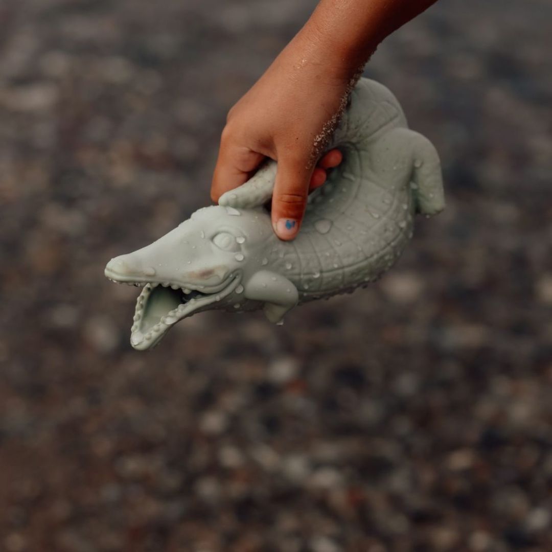 Hånd holder grøn krokodille-vandkande fra Scrunch i silikone, fås hos Nordic Simply