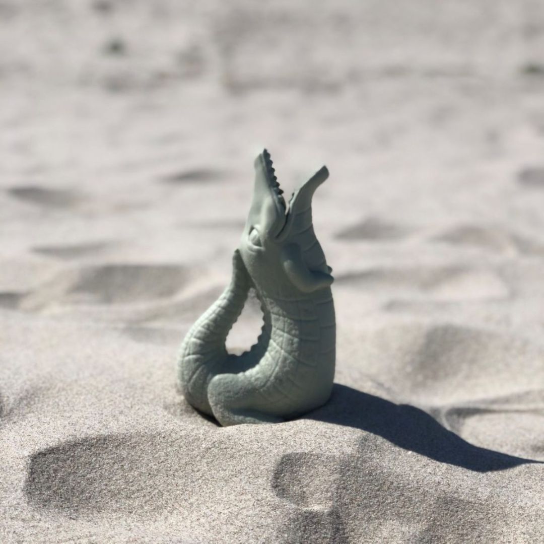 Grøn vandkande formet som en krokodille fra Scrunch, set i sand på strand, fås hos Nordic Simply