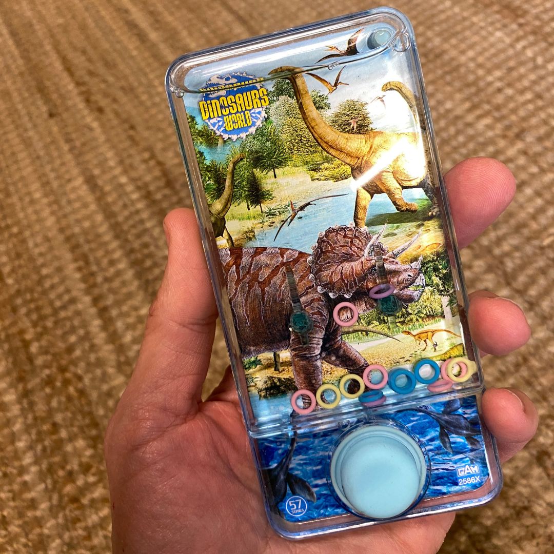 Hånd holder vandspil med dino, fint lille spil til rejser, bilture og flyrejse