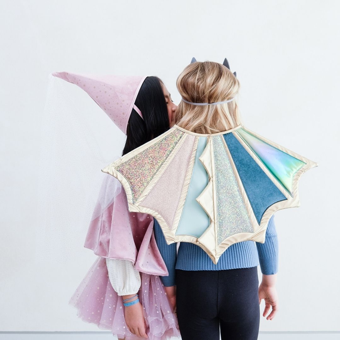 Pige hvisker i øret på pige med dragevinger i pastelfarver med glitter og guld til udklædning fra Mimi & Lula fås hos Nordic Simply