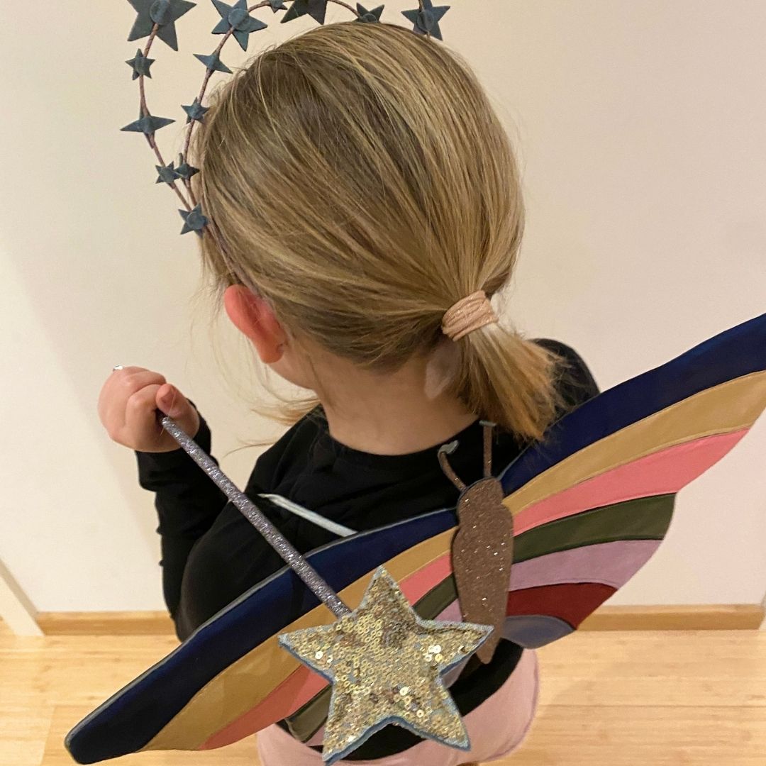 Pige set oppefra med guld tryllestav og sommerfuglevinger i multifarvet med guldglitter, smuk udklædning fra Mimi & Lula fås hos Nordic Simply