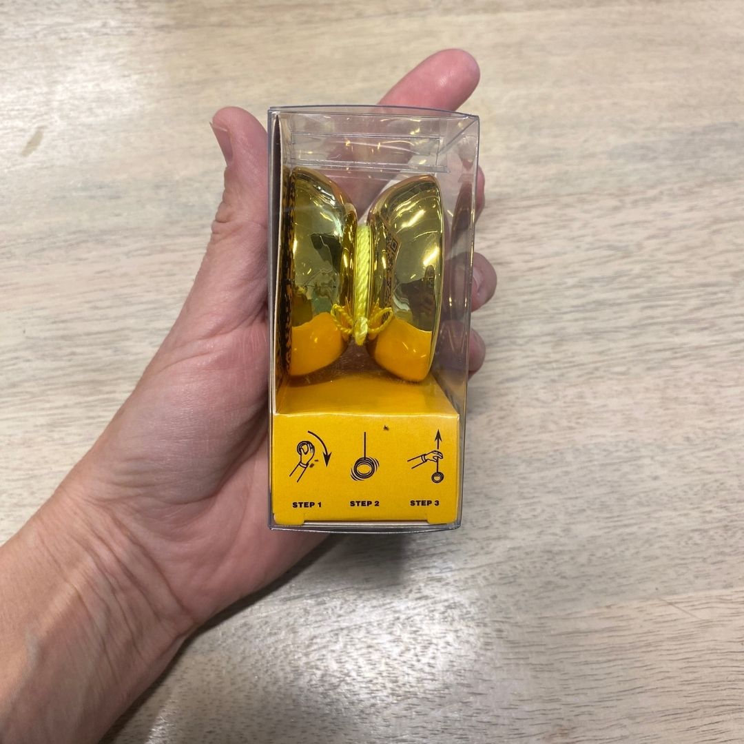 Hånd holder guldfarvet yoyo i æske fra siden til aktiv leg ude og inde for børn