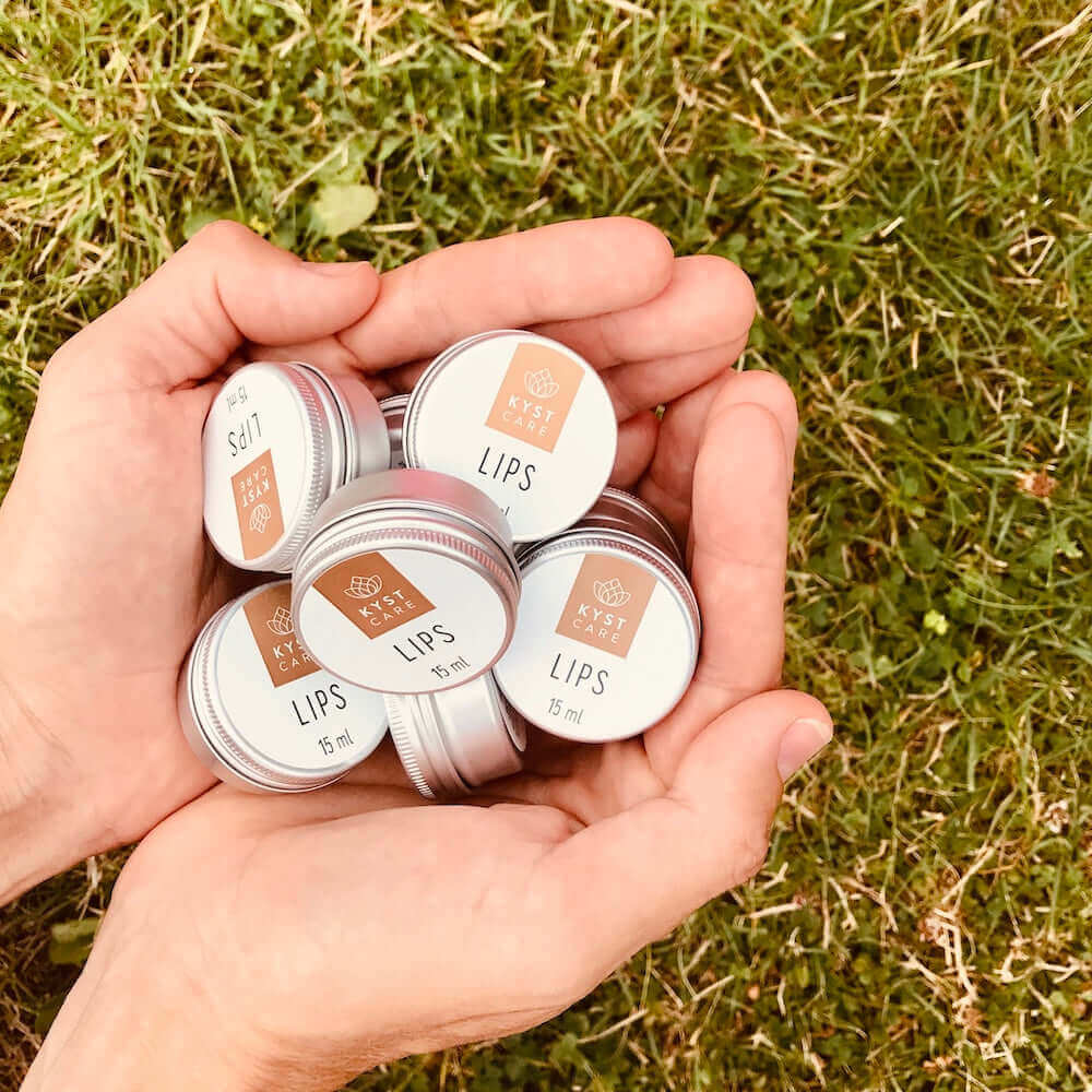 Hånd holder bøtter med Lips rød læbebalsam, naturlig dansk hudpleje fra Kyst Care fås hos Nordic Simply