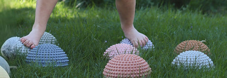 bare barnefødder går på sansesten i pastelfarver med knopper på græsplæne