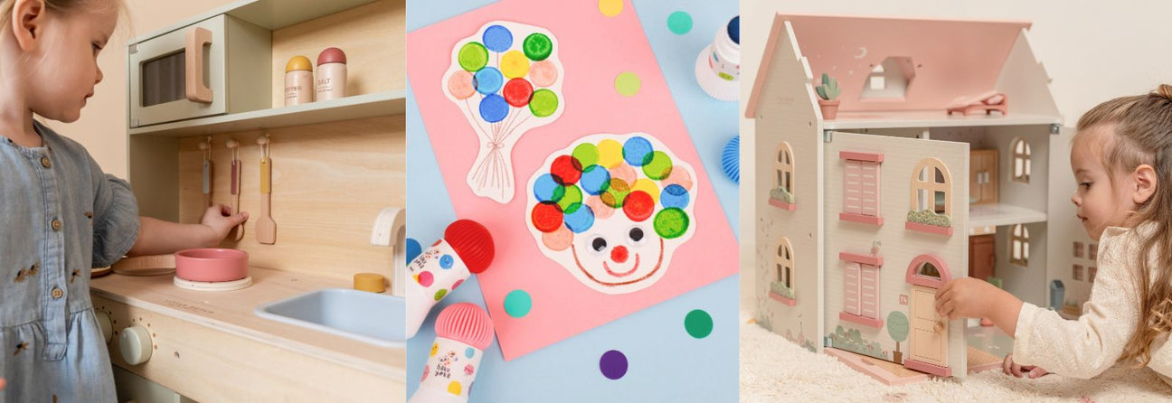 pige i legekøkken i træ, farverig tegning lavet med farvestempler, pige ligger på gulv med hænderne i stort lyst dukkehus med rosa tag, gode julegaver pige 3 år hos Nordic Simply