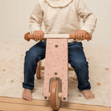 Barn kører på rosa trehjulet balancecykel i træ fra Little Dutch, ideel til at udvikle balance og koordination hos børn fra 18 måneder og op.