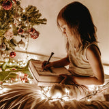 pige på 6-9 år sidder og tegner ved juletræ  - som illustration til adventskalender til børn hos Nordic Simply