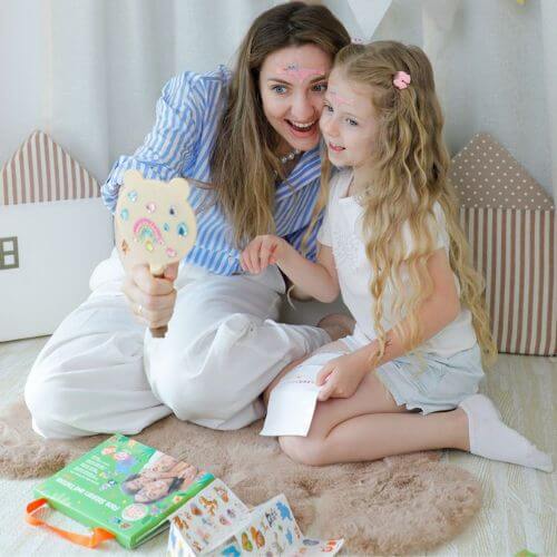 Mother and daughter enjoying face stickers and tattoos, smiling while looking in a mirror during playtime fun.