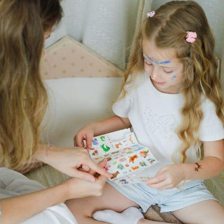 Girl excitedly choosing colorful animal face stickers and tattoos with a parent, enjoying creative playtime together.