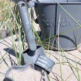 "jeg er blevet væk" armbånd til børn med navn og telefonnummer i antracit- her set på strand med strandlegetøj i samme farve