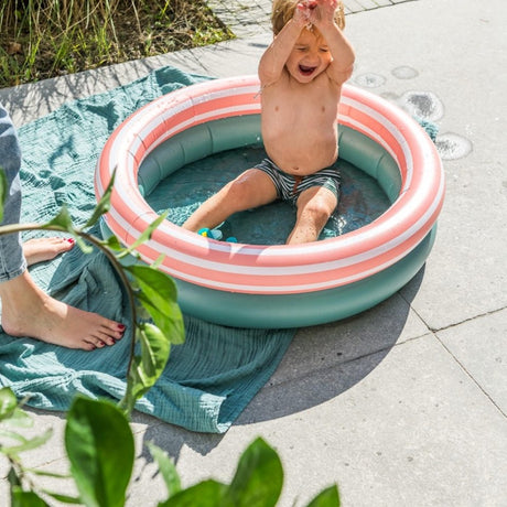 dreng sidder i lille rundt badebassin med to ringe, en grøn og en orange med hvide striber, bassinet har en diameter på 80 centimeter og er derfor til små børn under opsyn.
