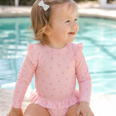pige ved pool i pink badedragt med lange ærmer og pink motiver af blomster, badedragt med UV40 beskyttelse.