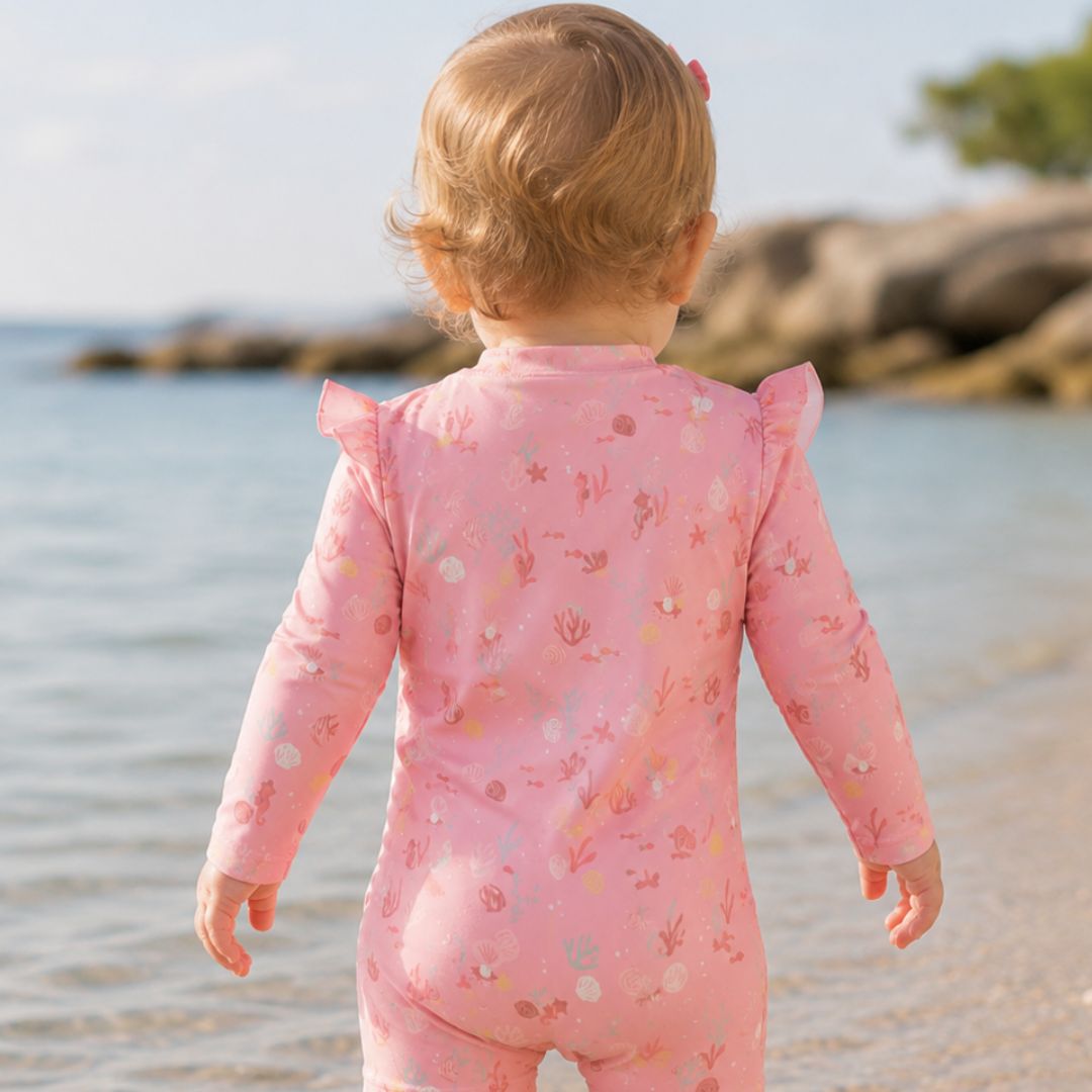 baby på strand med pink badedragt med lange ærmer og UV beskyttelse, set bagfra