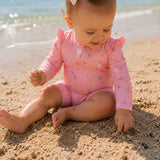 baby sidder på strand med pink badedragt med lange ærmer og UV beskyttelse