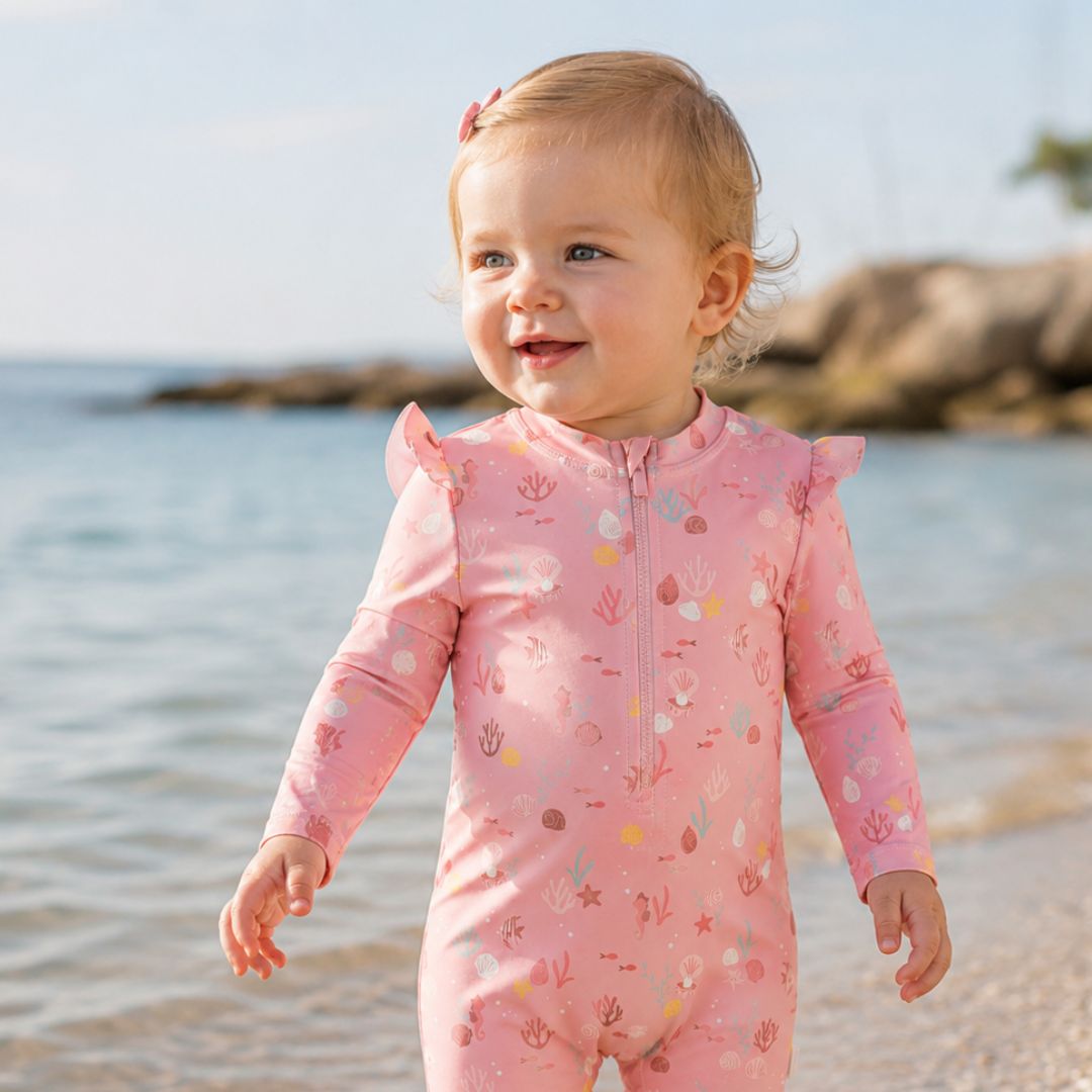 baby på strand med pink badedragt med lange ærmer og UV beskyttelse, set forfra