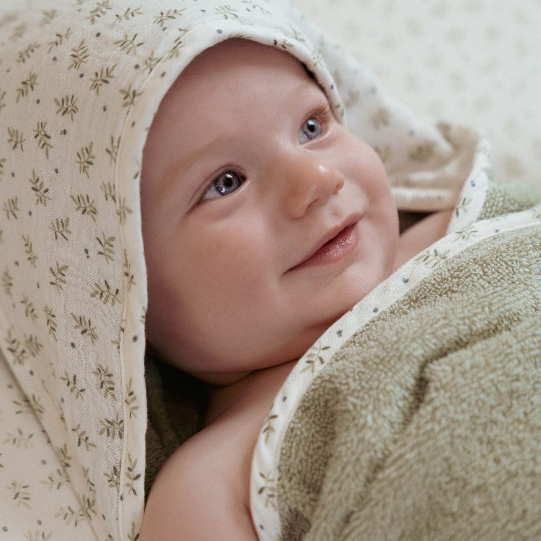 Baby svøbt i grønt og hvidt badehåndklæde i økologisk frotté med hætte og motiver af blåbærblade på hætten.