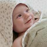Baby svøbt i grønt og hvidt badehåndklæde i økologisk frotté med hætte og motiver af blåbærblade på hætten.