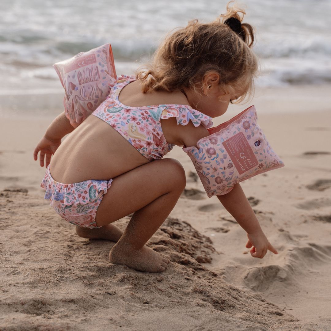 Pige ved strand med rosa badevinger på. Svømmevinger til børn 2-6 år, op til 30 kilo.