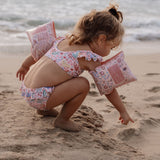 Pige ved strand med rosa badevinger på. Svømmevinger til børn 2-6 år, op til 30 kilo.